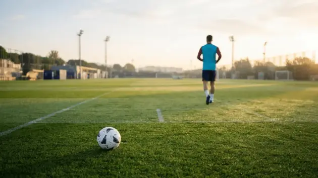 Barcelona training ground with football on grass and player silhouette returning to training