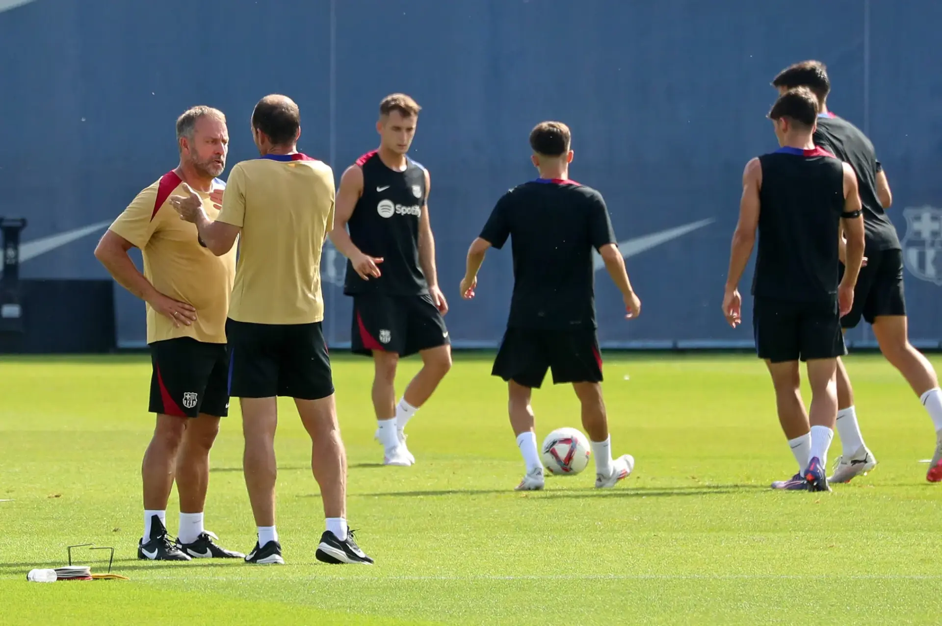 Barcelona players training on the pitch with coaches discussing tactics.