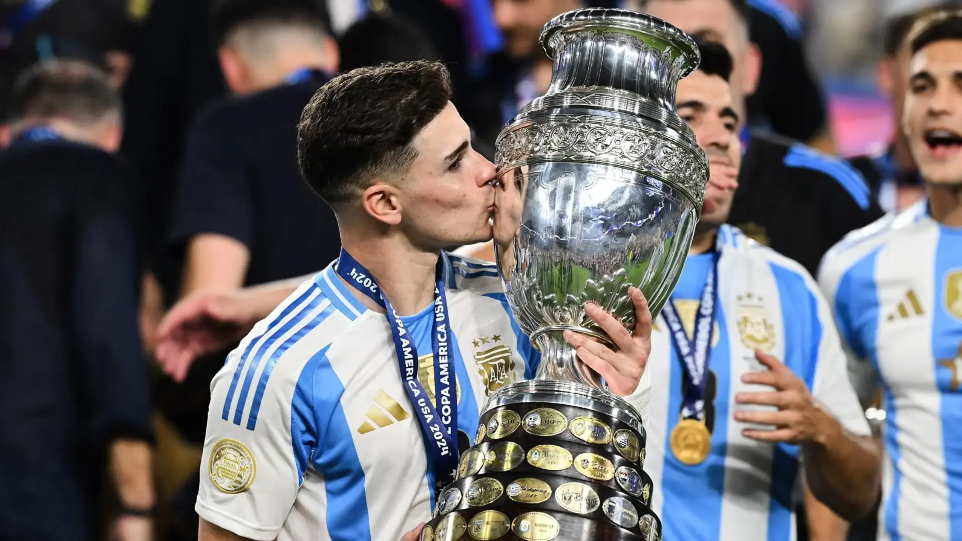 Julian Alvarez kisses the Copa America trophy while celebrating with teammates.