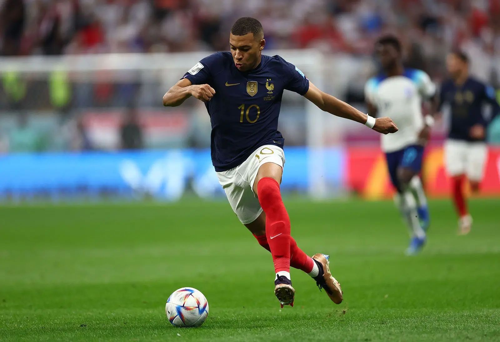 Kylian Mbappé in France national team jersey performing a kick on the field.