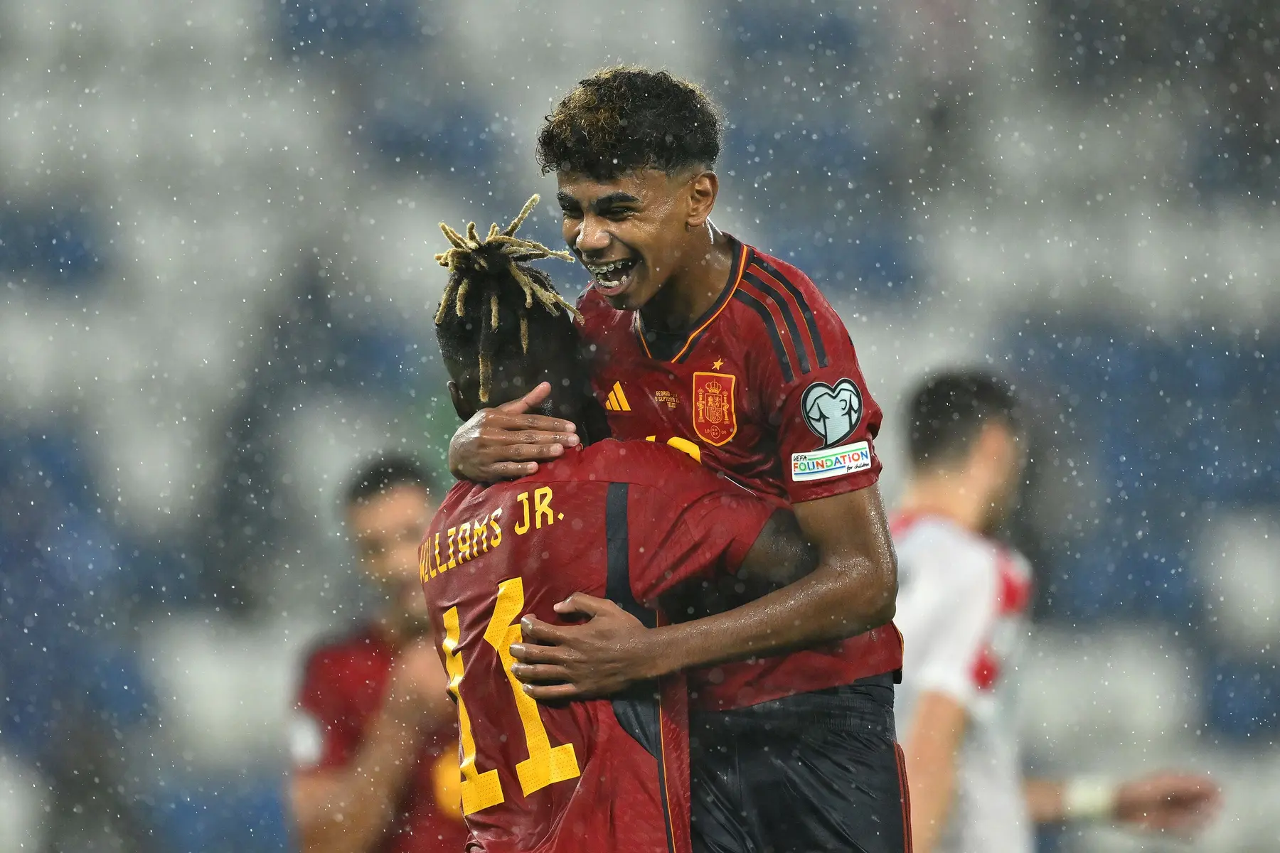 Two Spain national team players celebrating in the rain during a match.