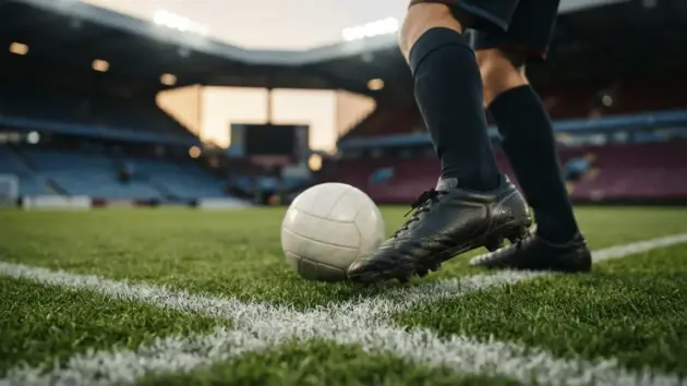 Football striker's boots on stadium grass under floodlights with penalty box line