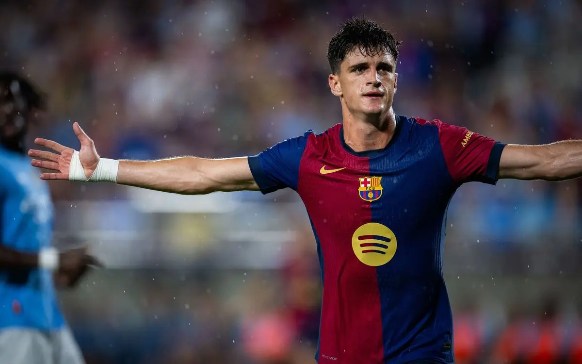 FC Barcelona player Frenkie de Jong in a blue and red striped jersey with arms outstretched on the pitch