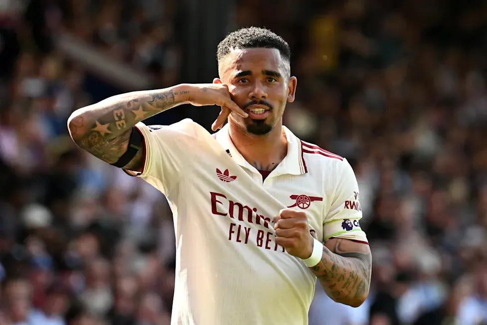Gabriel Jesus wearing an Arsenal home kit and gesturing towards his head during a match.