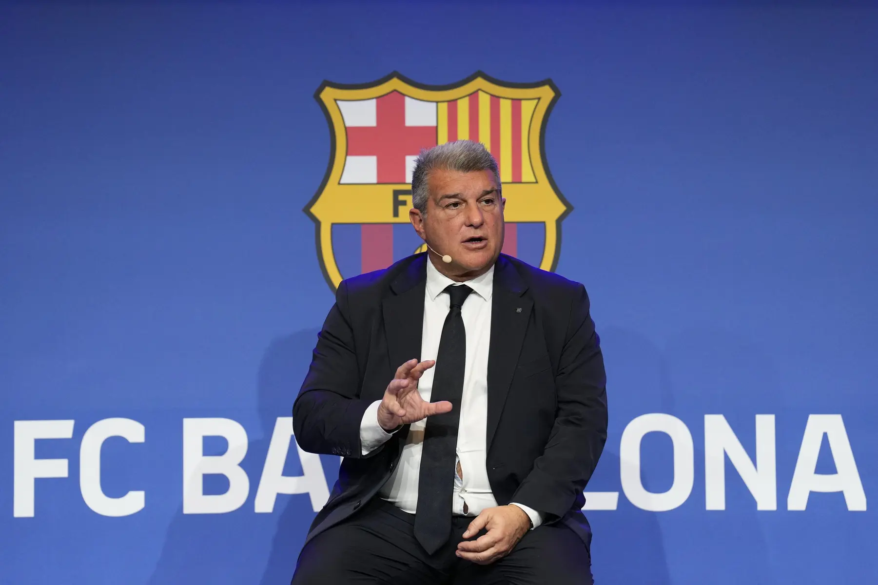 Joan Laporta, President of FC Barcelona, speaking at a press conference with the club's crest in the background
