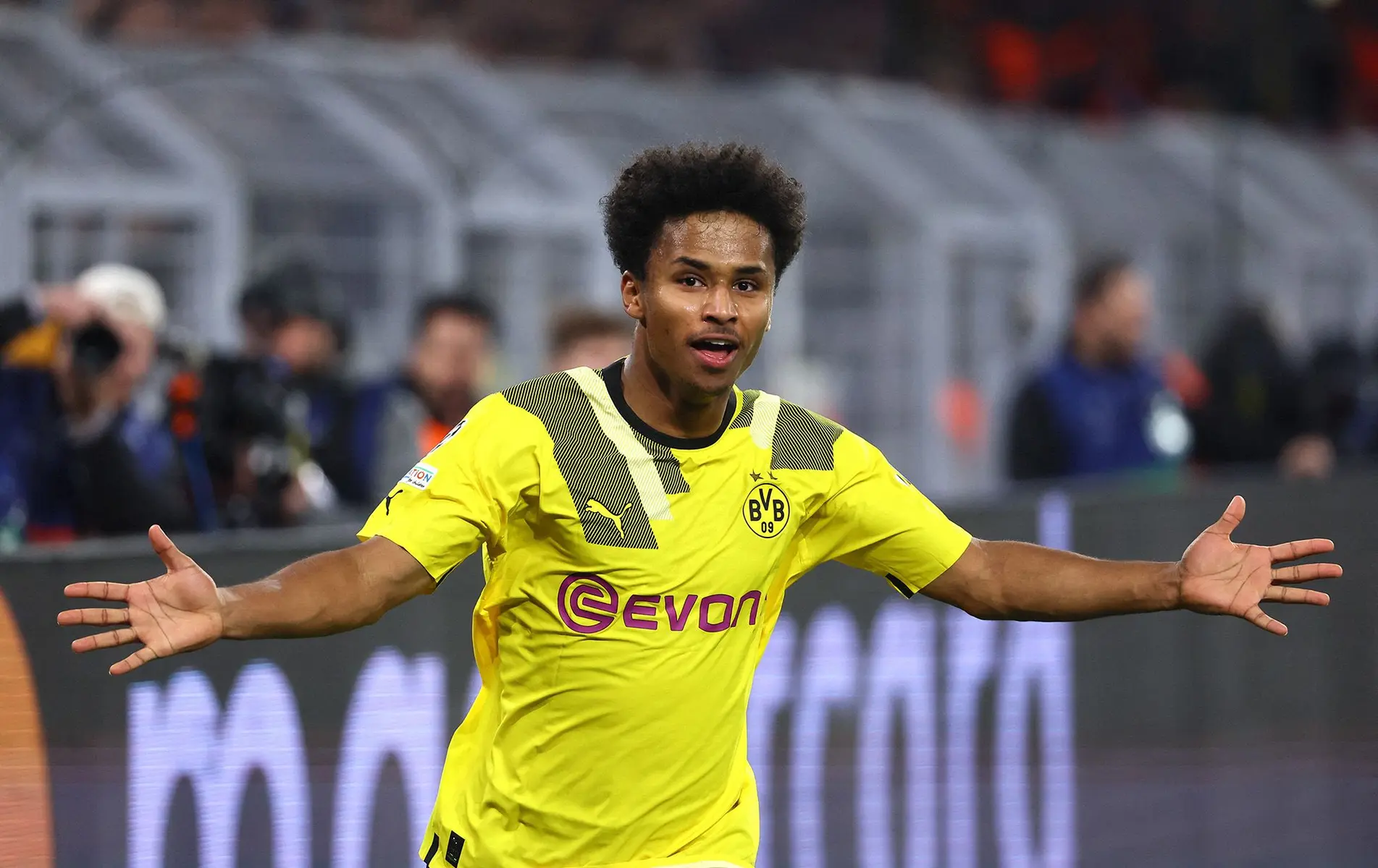 Karim Adeyemi celebrating in a yellow Borussia Dortmund kit with arms outstretched