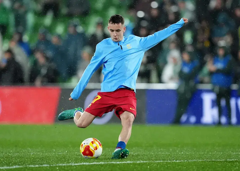 Marc Casadó in a light blue training top and red shorts kicking a soccer ball on a pitch