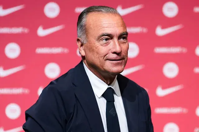 Portrait of Rafa Yuste wearing a dark suit and tie against a red branded background