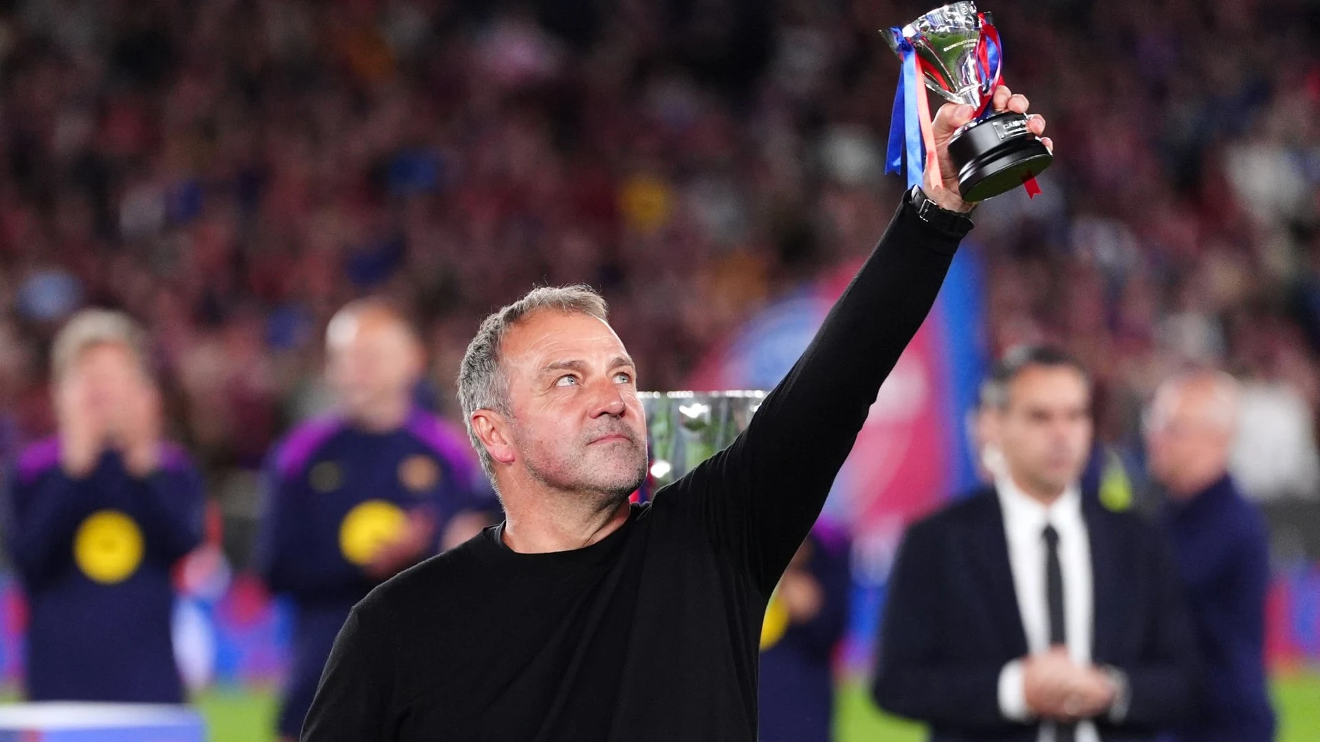 Hansi Flick holding up a trophy while celebrating on a football pitch.