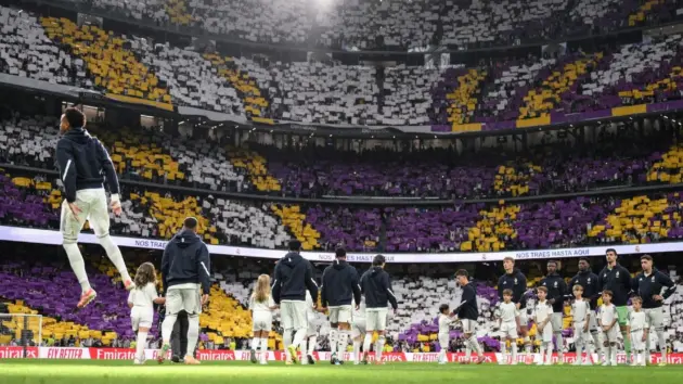Real Madrid players and children standing on the pitch in front of a crowded stadium with choreographed banners