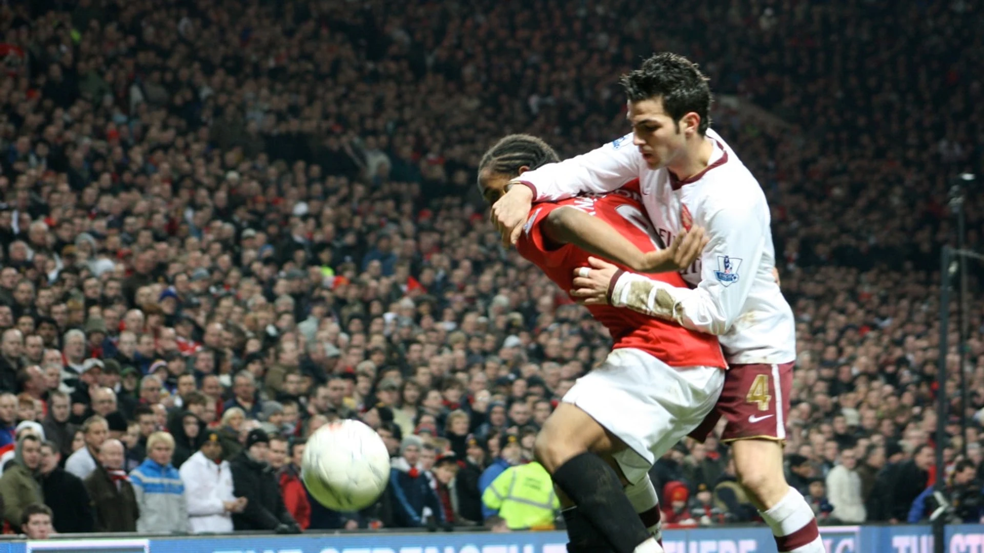 Cesc Fàbregas in a white kit during a football match, contending for the ball with another player.