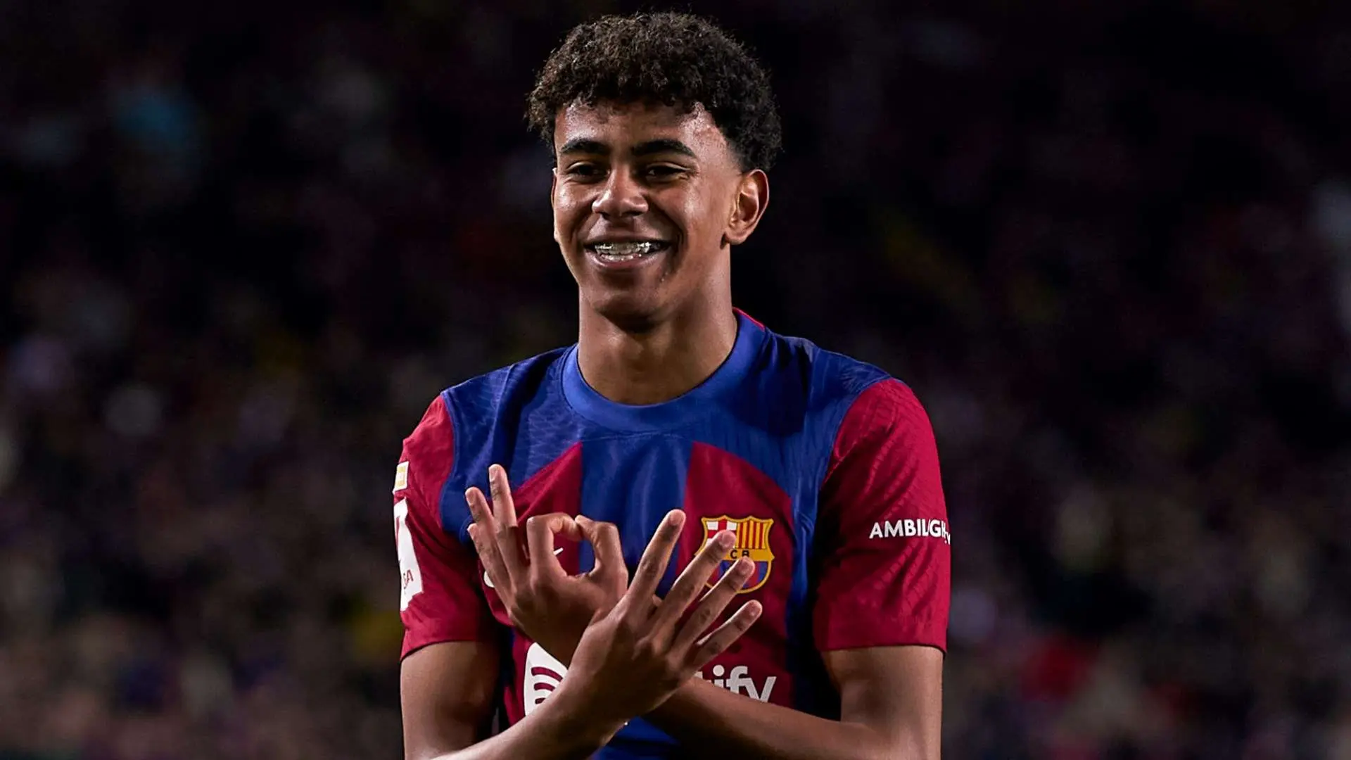 Lamine Yamal smiling and making a hand gesture while wearing the FC Barcelona home kit