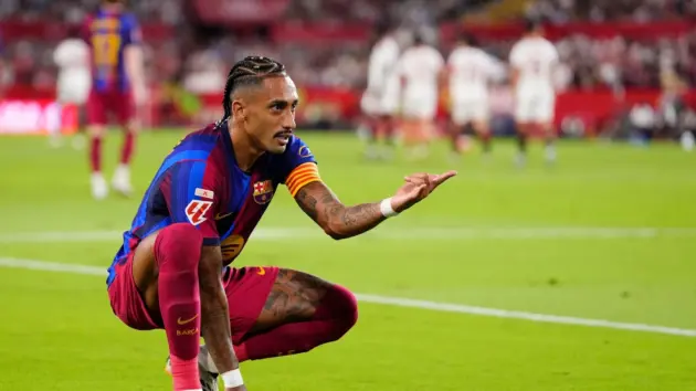 Raphinha in a Barcelona kit kneeling on the pitch and pointing during a match.