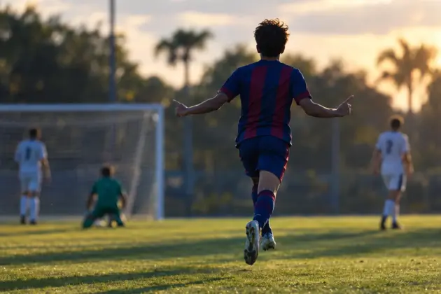 Anonymous youth footballer celebrates a comeback goal on an academy pitch in blue and claret colors