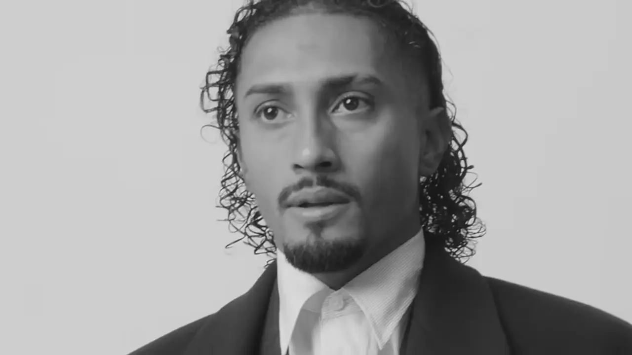 Black and white portrait of Raphinha wearing a suit and collared shirt.